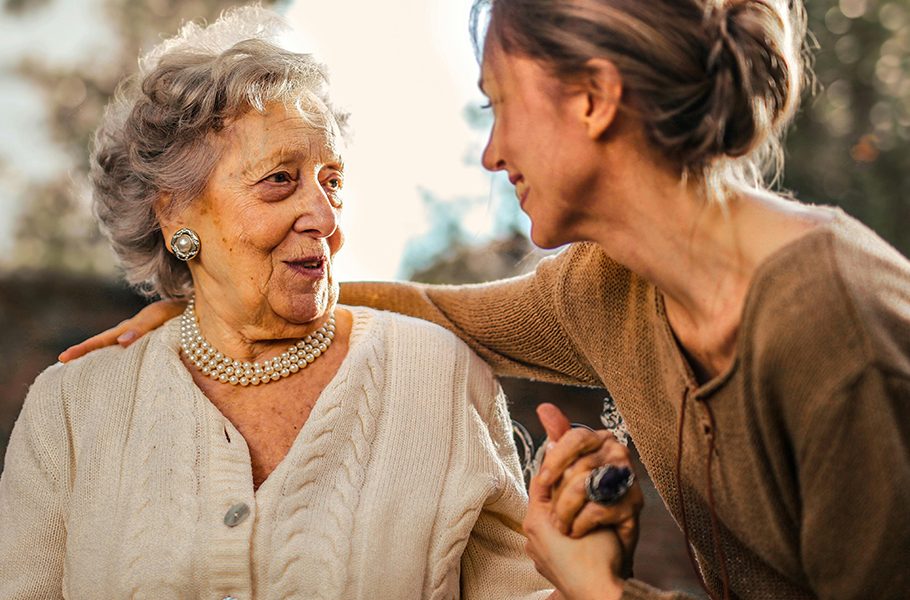 Elderly woman and younger woman smiling in a warm, outdoor setting.