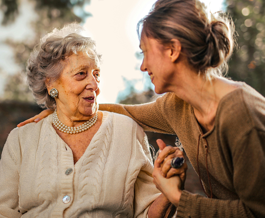 Elderly woman and younger woman smiling in a warm, outdoor setting.
