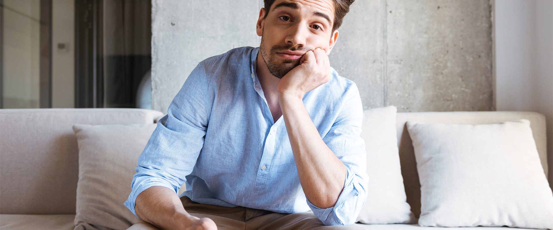 Man sitting on a couch looking bored, holding a remote control.