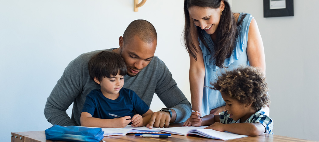 Family helping children with homework together at table.