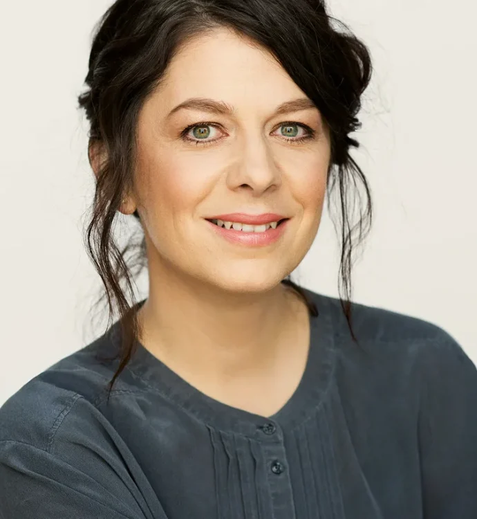 Smiling woman with dark hair in dark blouse, studio portrait on light background.