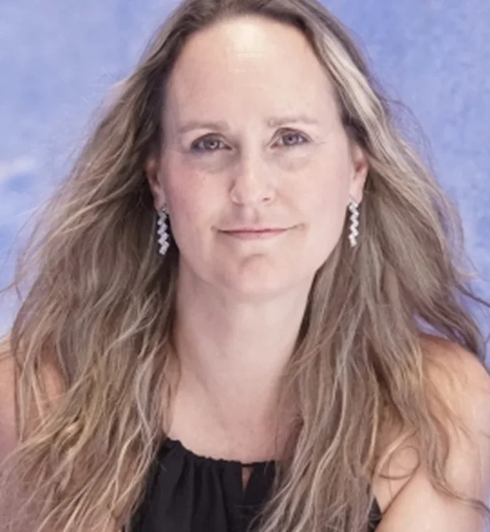 Woman with long hair and earrings smiling against a blue background.