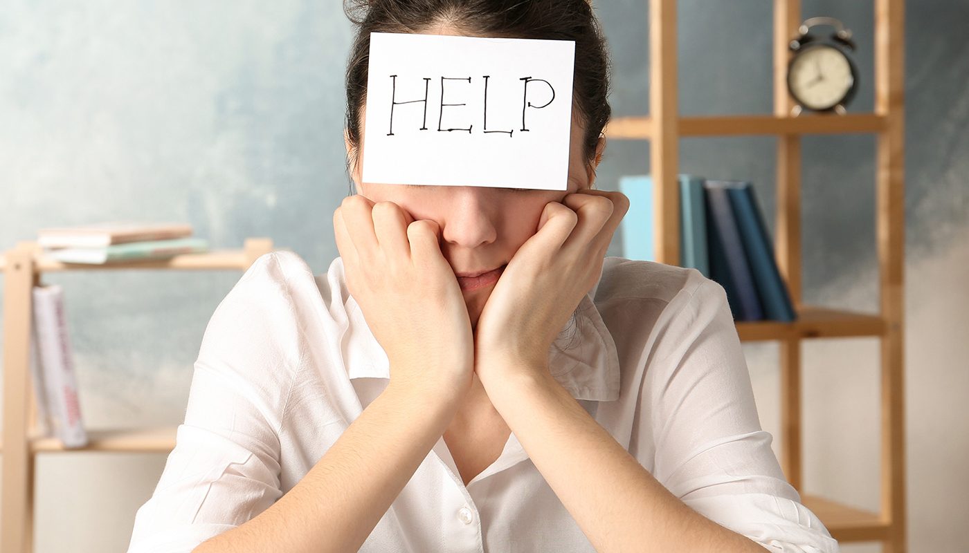 Stressed person with HELP note on forehead at desk, seeking assistance or relief.
