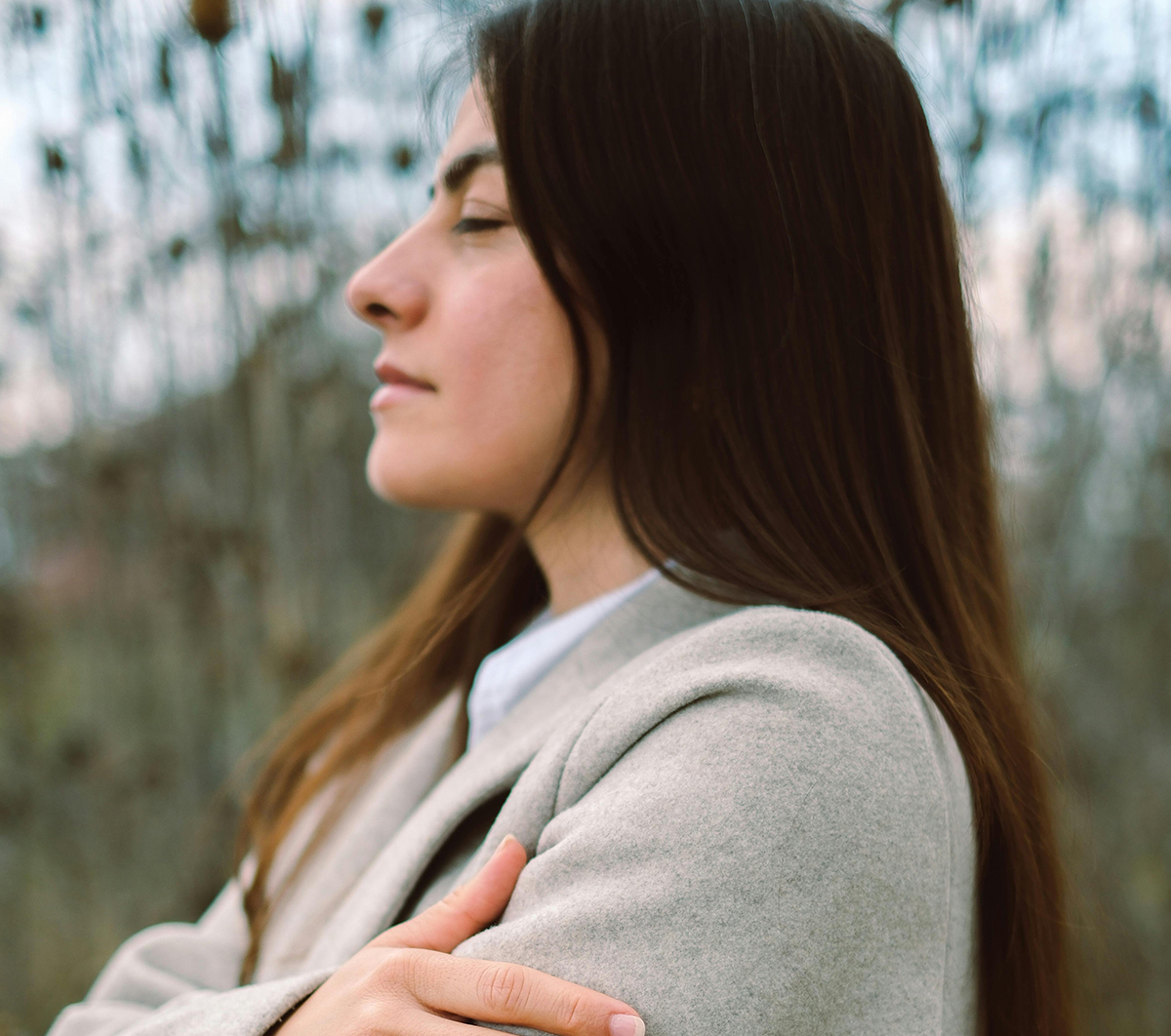 Woman with closed eyes in nature, wearing a gray coat, side profile view