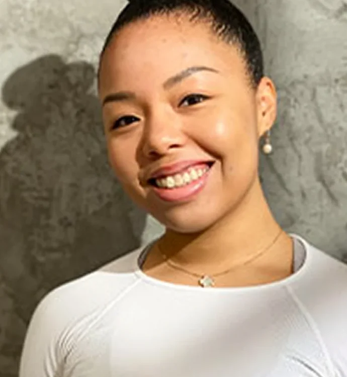 Smiling person in white top standing against a textured gray wall.