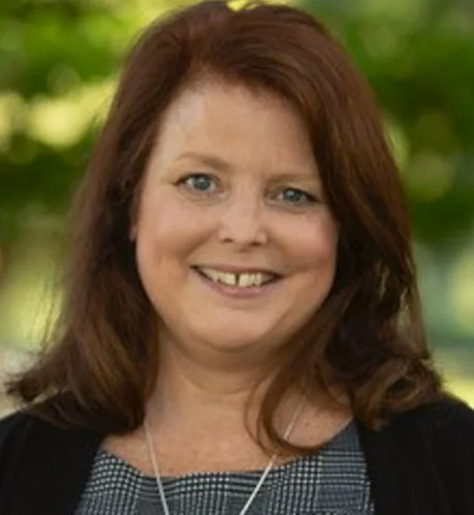 Smiling woman with brown hair wearing a patterned top, outdoor professional headshot