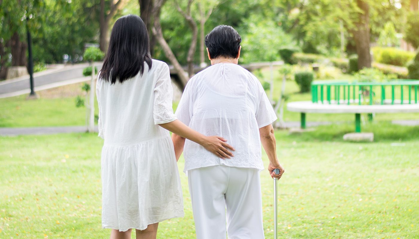 Woman assisting elderly lady with a cane through a park.