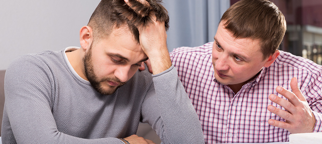 Man comforting a stressed colleague holding his head during a serious conversation indoors