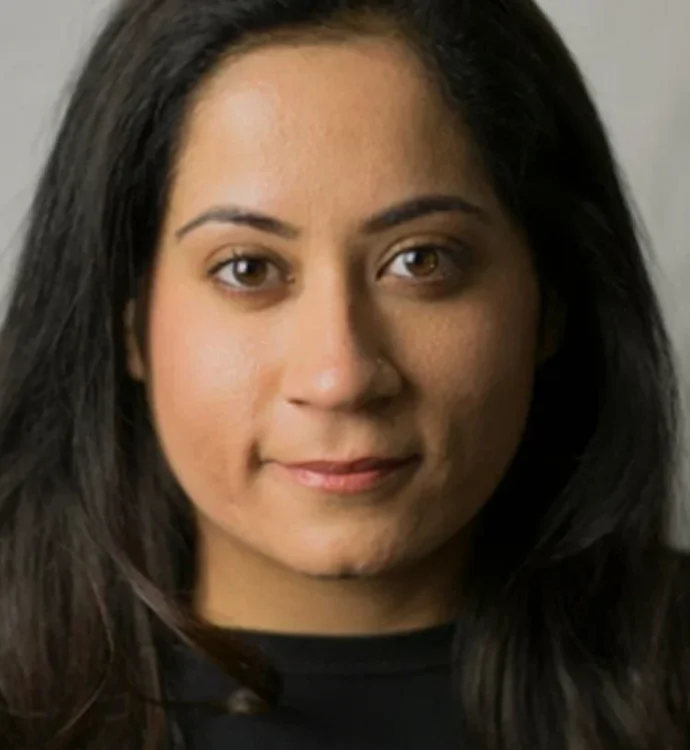 Portrait of a woman with long dark hair and neutral expression on a gray background.