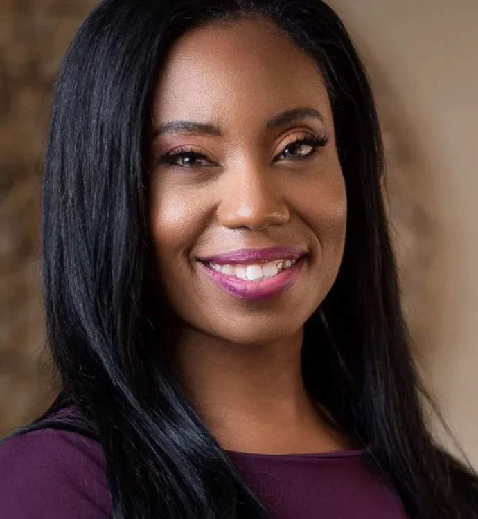 Smiling woman with long black hair and purple lipstick in a professional setting.