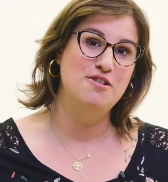 Portrait of a woman with glasses, brown hair, wearing a floral top and gold earrings.