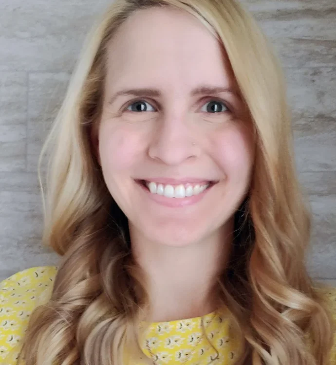 Smiling woman with blonde hair and yellow floral top against a neutral background.