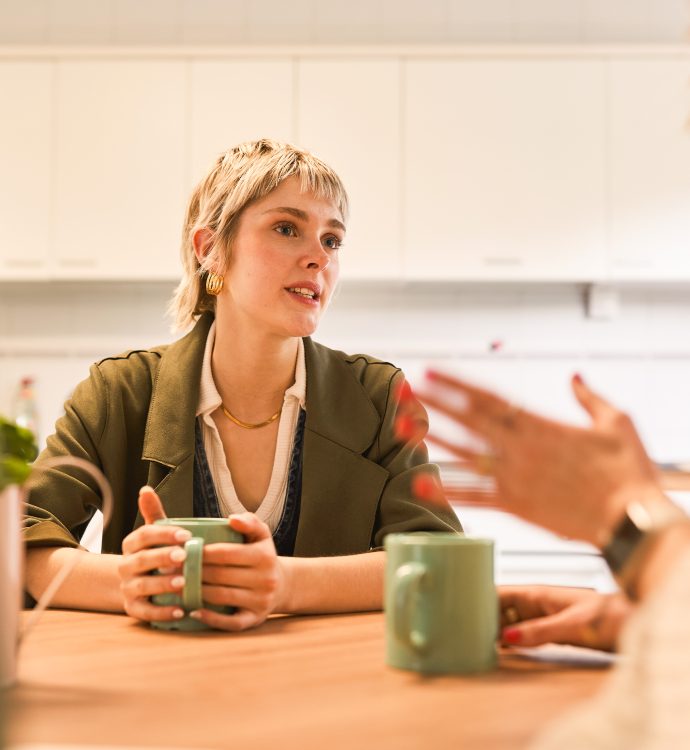 Two women having a friendly conversation over coffee in a cozy kitchen setting.
