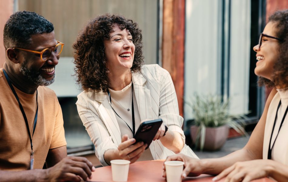 Group of three people enjoying a coffee break while smiling and chatting outdoors.