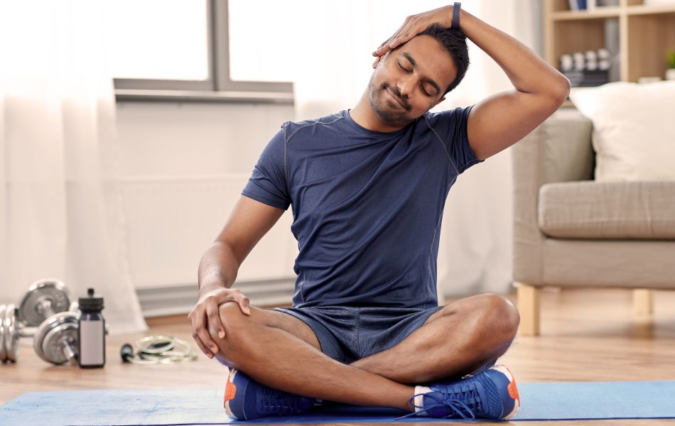 Man doing yoga neck stretch at home on exercise mat.