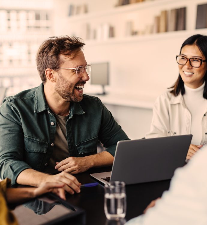Team meeting with diverse group laughing around laptop in modern office.
