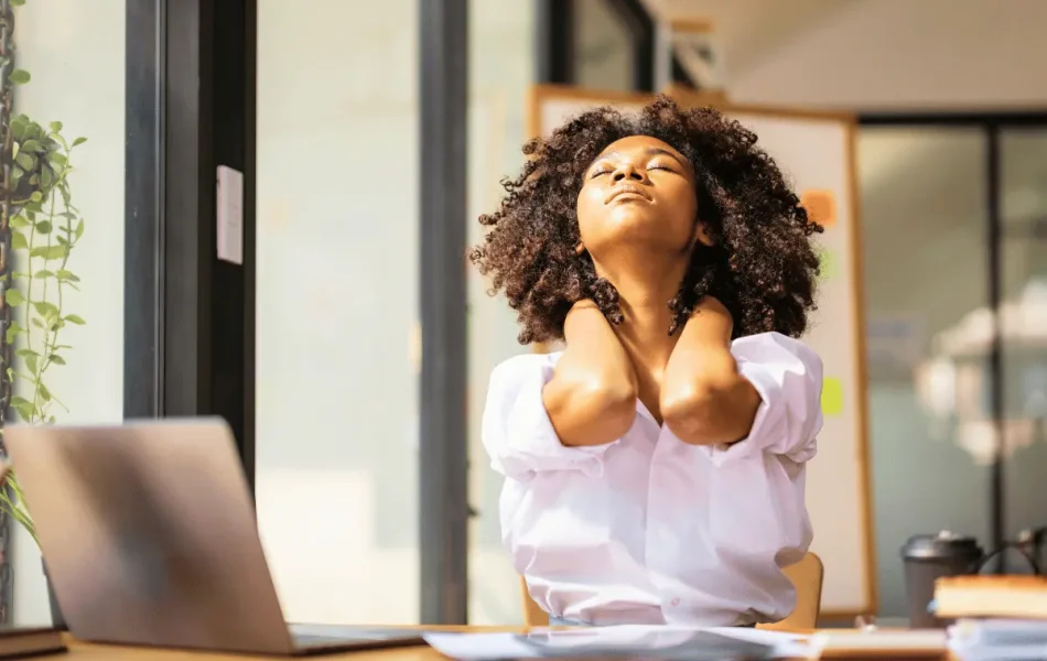 A woman at her desk holding her neck in discomfort, illustrating back and musculoskeletal pain at work.