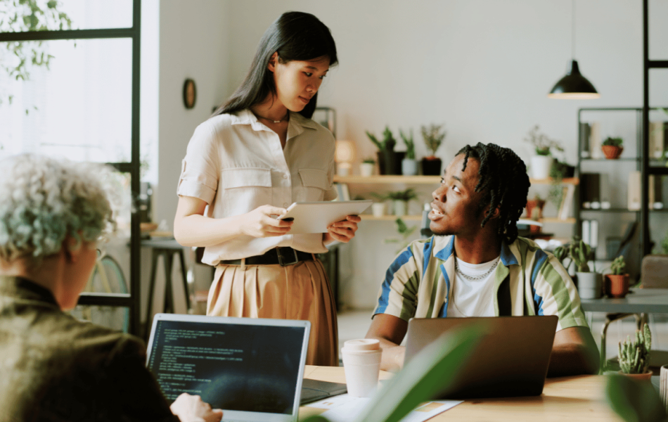 Two young professionals in a modern office discussing work around laptops, representing Gen Z employees and empathy-driven collaboration at work