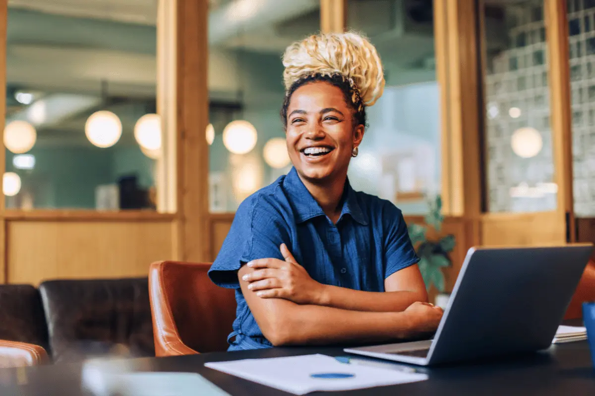 HR leader smiling while reviewing open enrollment communication materials on a laptop in a modern office.