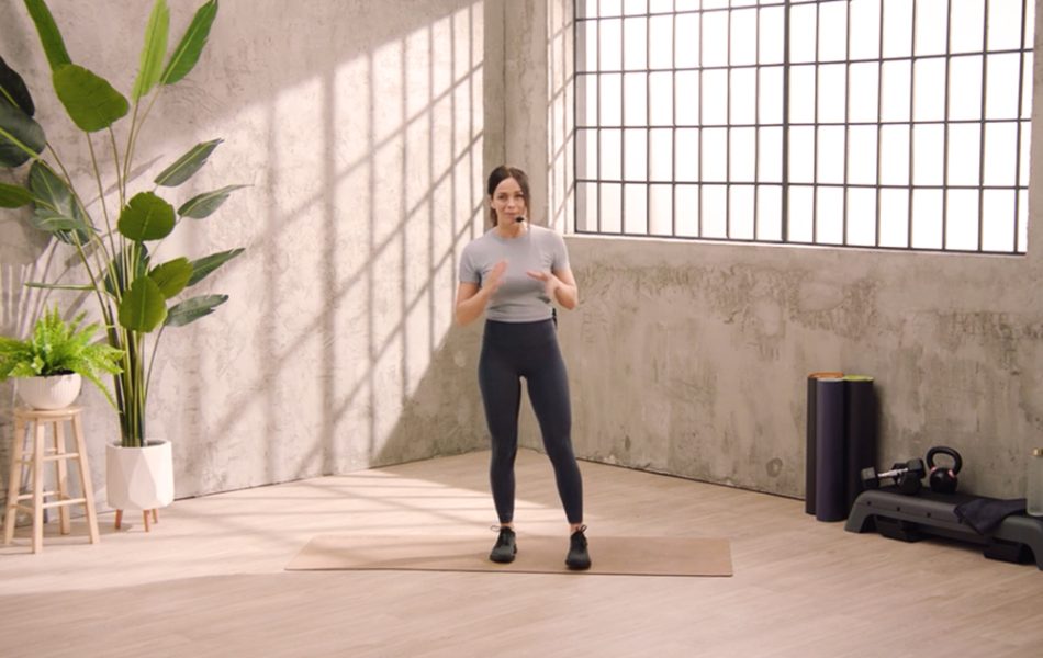 Fitness trainer leading a workout session in a bright, modern studio with large windows.