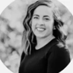 Smiling person in a black top with wavy hair, outdoors with blurred background.