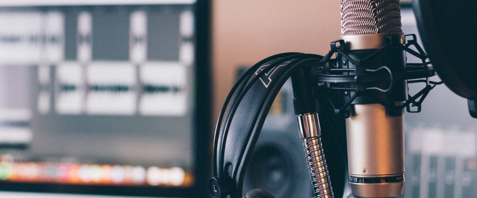 Microphone and headphones in a recording studio with computer screen in background.
