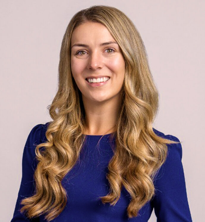 Smiling woman with long blonde hair in a blue top, portrait on a neutral background.