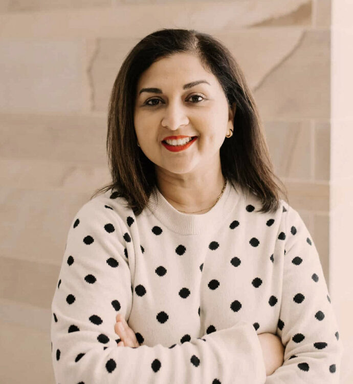 Smiling woman in polka dot sweater, arms crossed, standing against a neutral background.