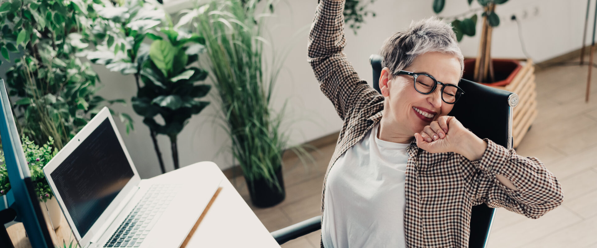 Person joyfully stretching in home office surrounded by lush indoor plants.