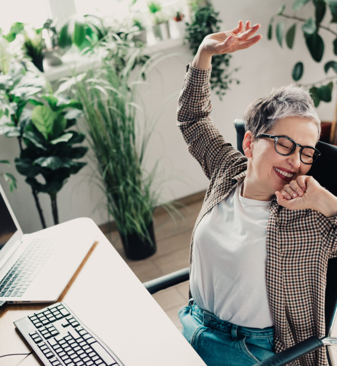 Person joyfully stretching in home office surrounded by lush indoor plants.