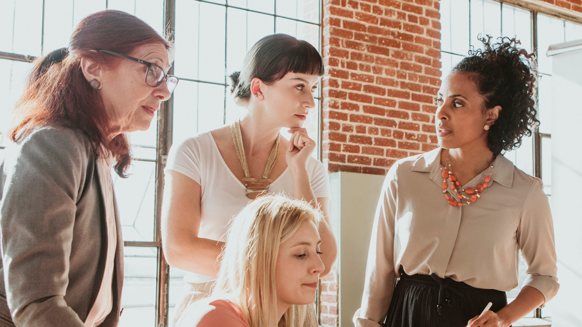 Women collaborating in a modern office with brick walls and sunlight.