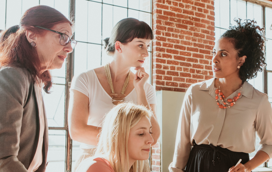Women collaborating in a modern office with brick walls and sunlight.